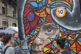 Bunte Graffiti-Wand mit Vogel- und Frauengesicht, mehrere Menschen davor.