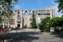 Historisches Gebäude mit spitzem Dach, Bäumen und blauem Himmel im Hintergrund.