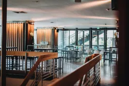 Modernes, lichtdurchflutetes Café mit Holzmöbeln und großen Fenstern.