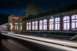 Beleuchtetes Backsteingebäude bei Nacht mit Lichtspuren auf der Straße.