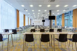 Moderner, heller Konferenzraum mit vielen leeren Tischen und Stühlen.