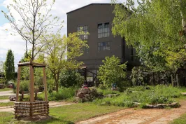 Großes graues Gebäude hinter grünem Garten mit Bäumen und Blumen.