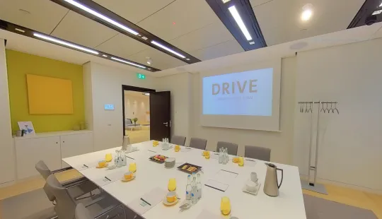 Konferenzraum mit großem Tisch, Getränken, Snacks und Präsentation mit Text "DRIVE".