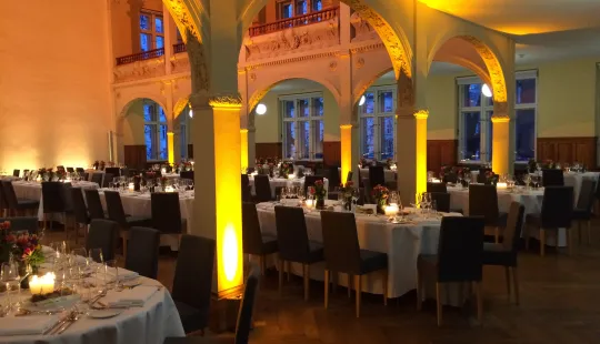 Elegant gedeckter Festsaal mit runden Tischen und warmem Licht.