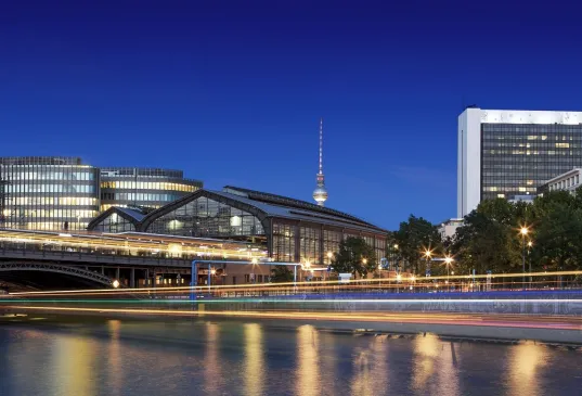 Berliner Stadtansicht bei Nacht mit beleuchteten Gebäuden und Fernsehturm im Hintergrund.
