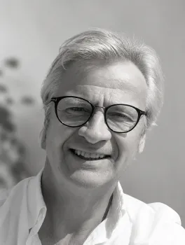 Schwarz-weiß-Foto eines lächelnden Mannes mit Brille und grauem Haar.