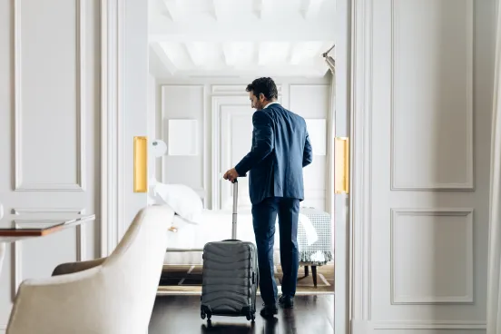 Mann im Anzug betritt mit Rollkoffer ein elegantes Hotelzimmer.